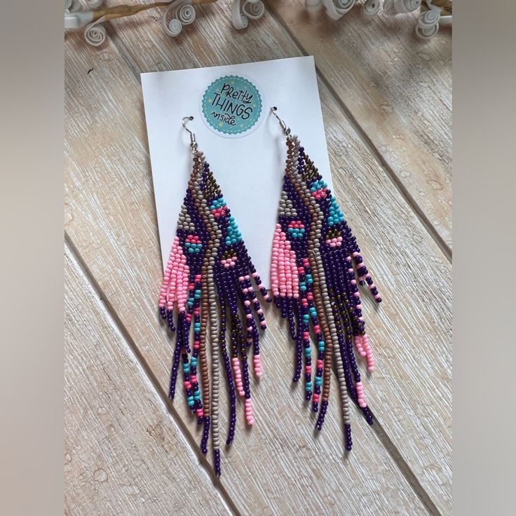 a pair of pink and blue beaded earrings sitting on top of a piece of paper