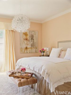 a white bed sitting in a bedroom next to a chandelier over a window