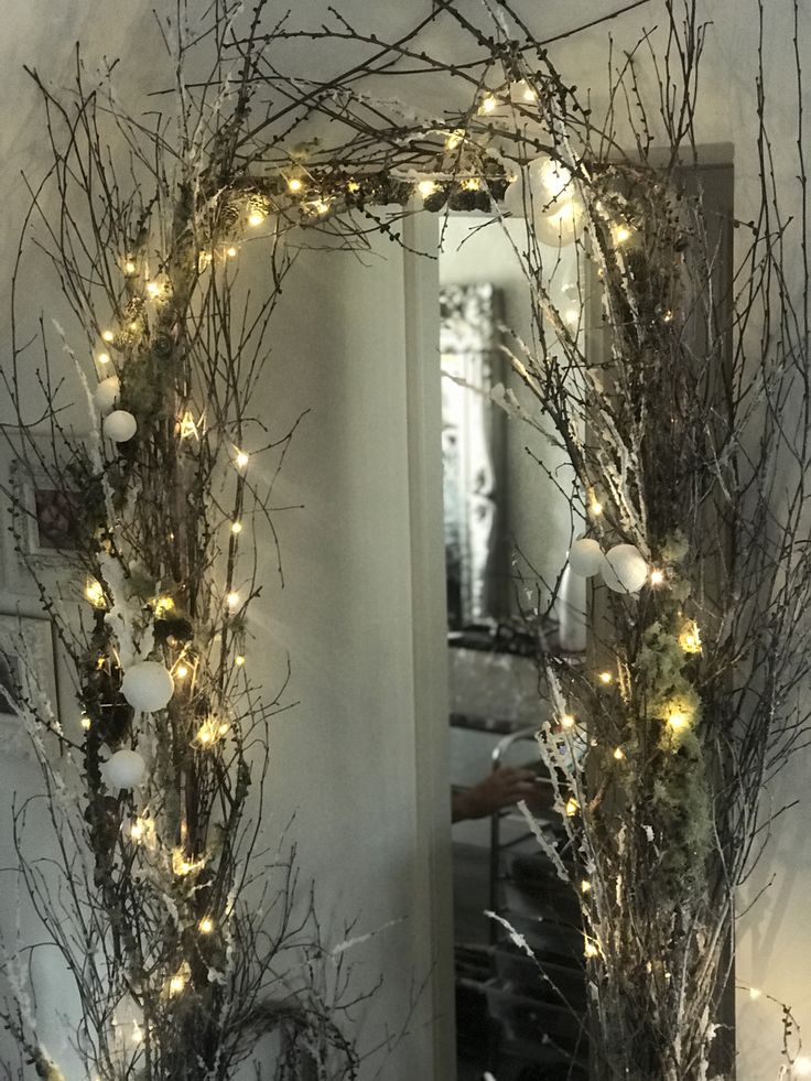 a mirror that has some branches and lights on it in front of a door way