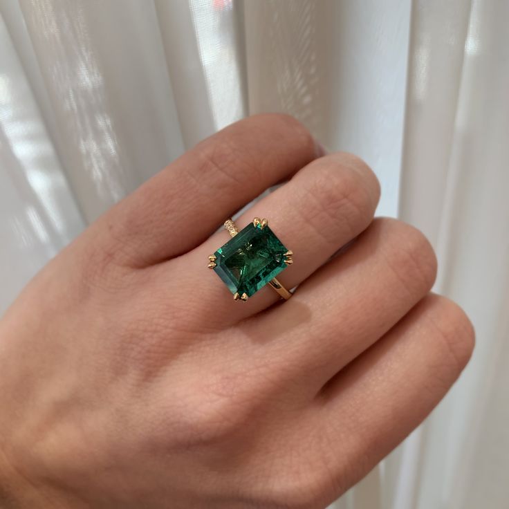 a woman's hand with a green ring on top of her finger and white curtains in the background