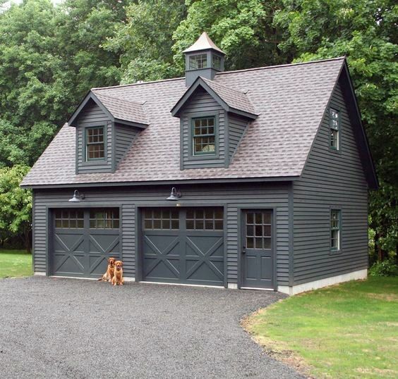 a dog sitting in front of a large garage with two windows on the side of it