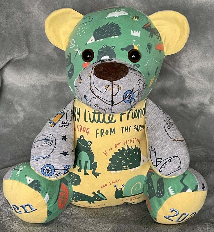 a teddy bear with green and yellow designs on it's face sitting in front of a gray background