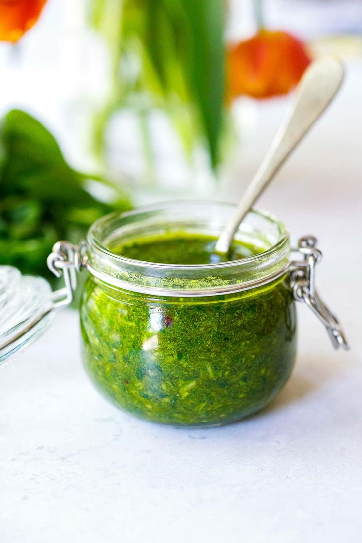 a jar filled with green pest sitting on top of a table next to some flowers