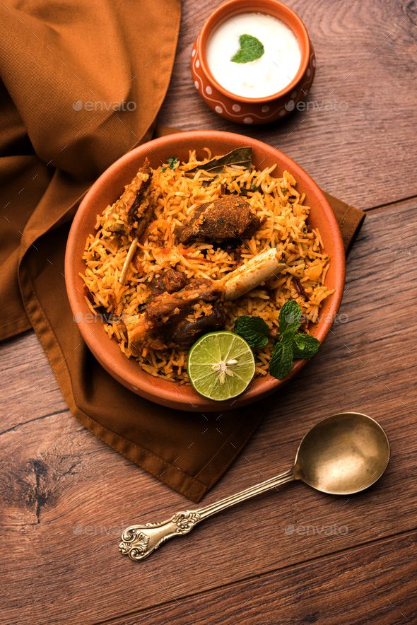 a bowl filled with rice and meat on top of a wooden table next to a spoon