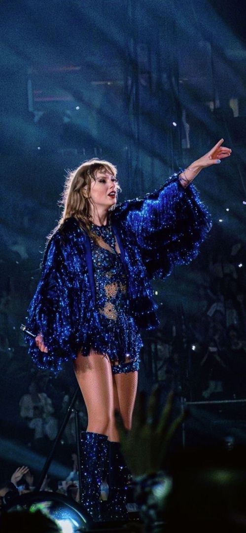 the singer is dressed in blue and has her arms out to catch the crowd's attention