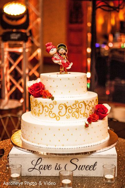 a white and gold wedding cake with red roses on top is sitting on a table