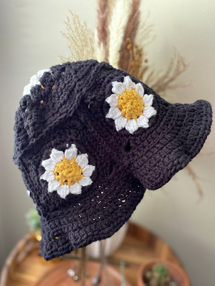 two crocheted hats with white and yellow flowers sitting on top of a table