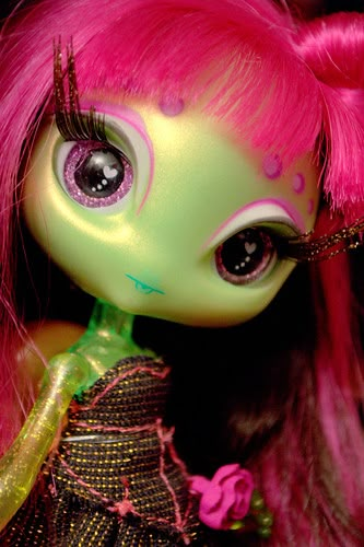 a close up of a doll with pink hair and big eyes wearing a green dress