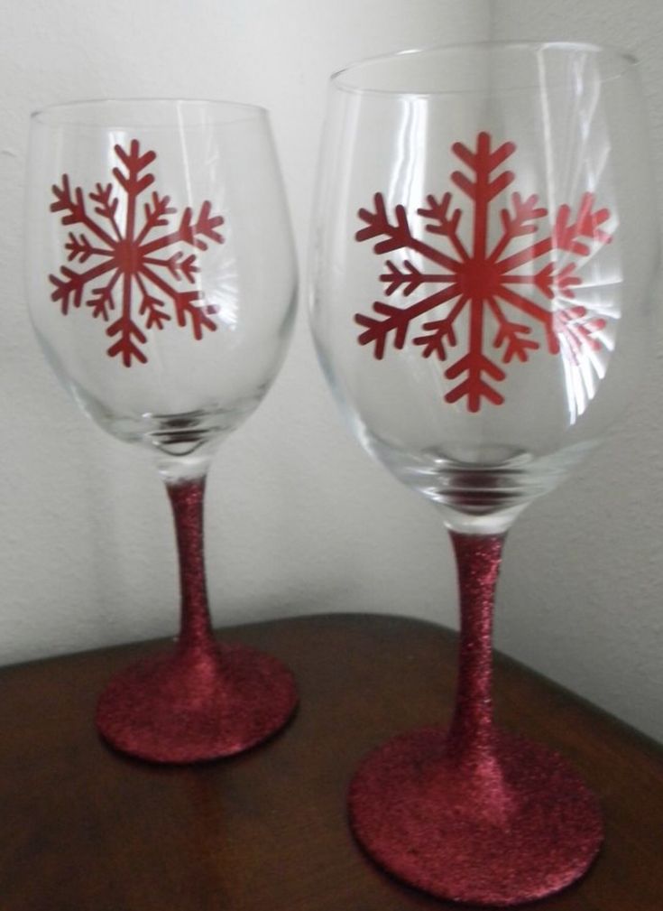 two wine glasses with red snowflakes painted on them sitting on a wooden table