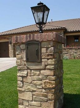 a stone mailbox in front of a house with a light on it's post