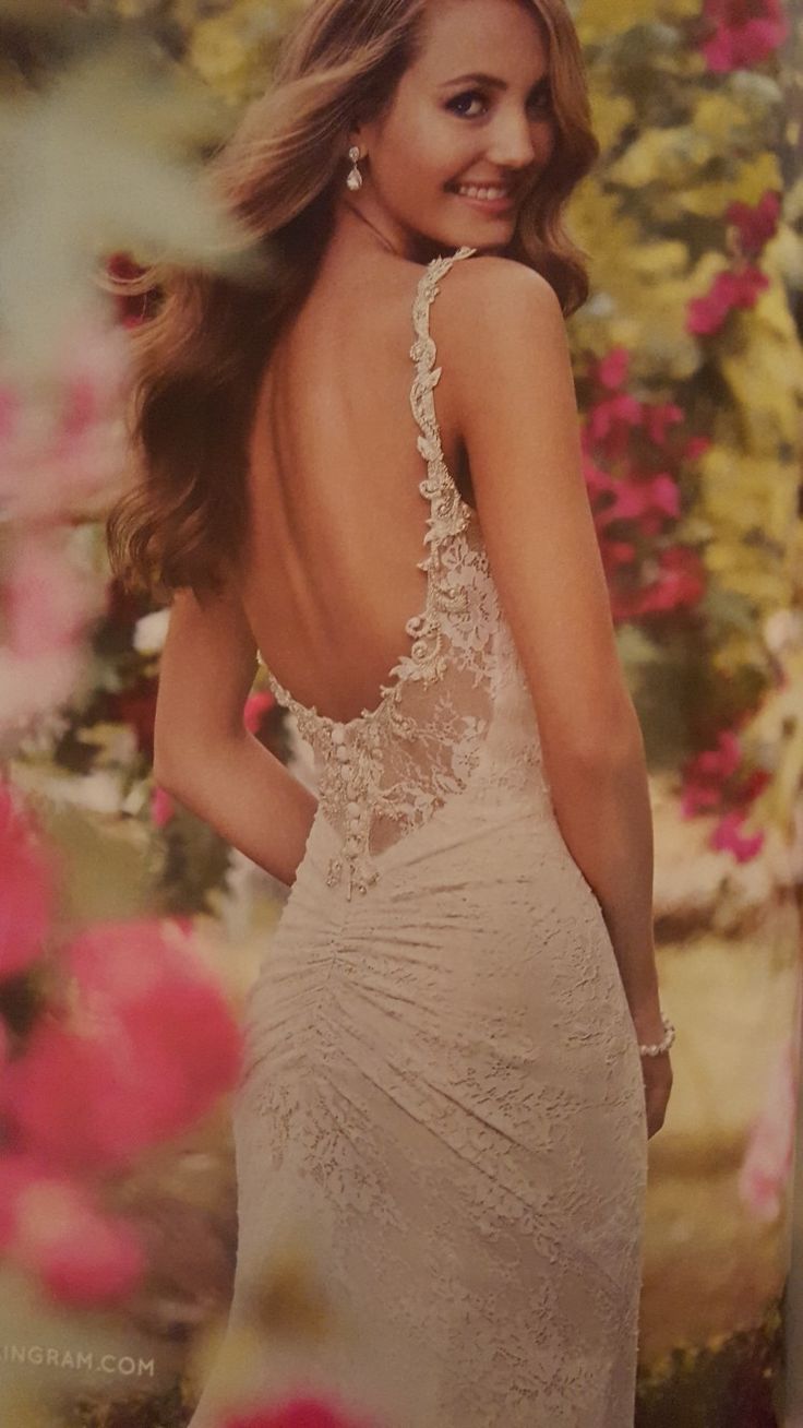 a beautiful woman in a white dress posing for a photo with flowers on the wall behind her