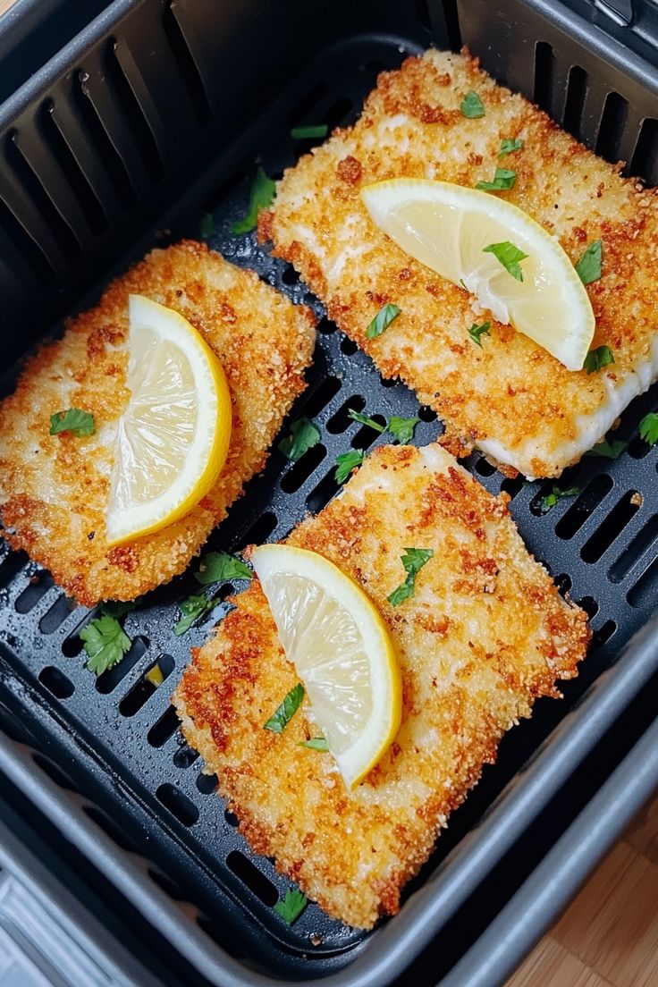 four fish fillets with lemon slices in a frying pan