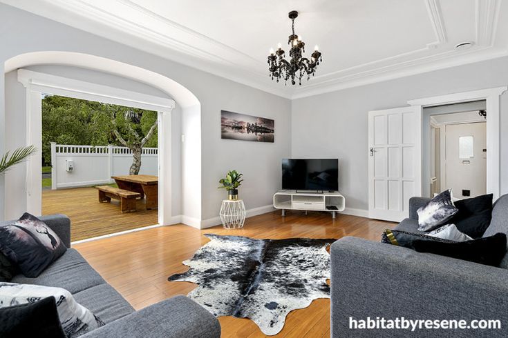 a living room filled with furniture and a chandelier hanging from the ceiling over a hard wood floor