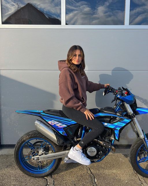 a woman sitting on top of a blue and black motorbike in front of a building