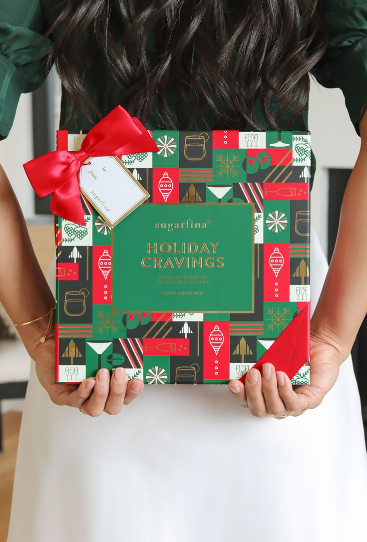 a woman holding a holiday wrappings box with red ribbon and green packaging in her hands