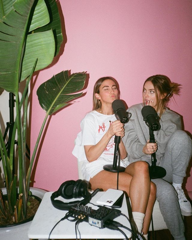 two women sitting next to each other in front of a pink wall talking into microphones