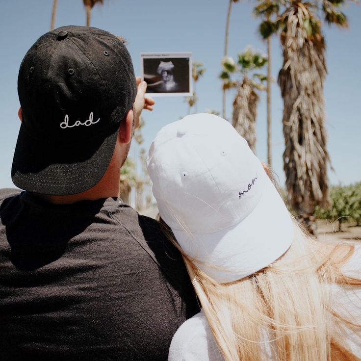 a man and woman taking a photo with their cell phone in front of palm trees