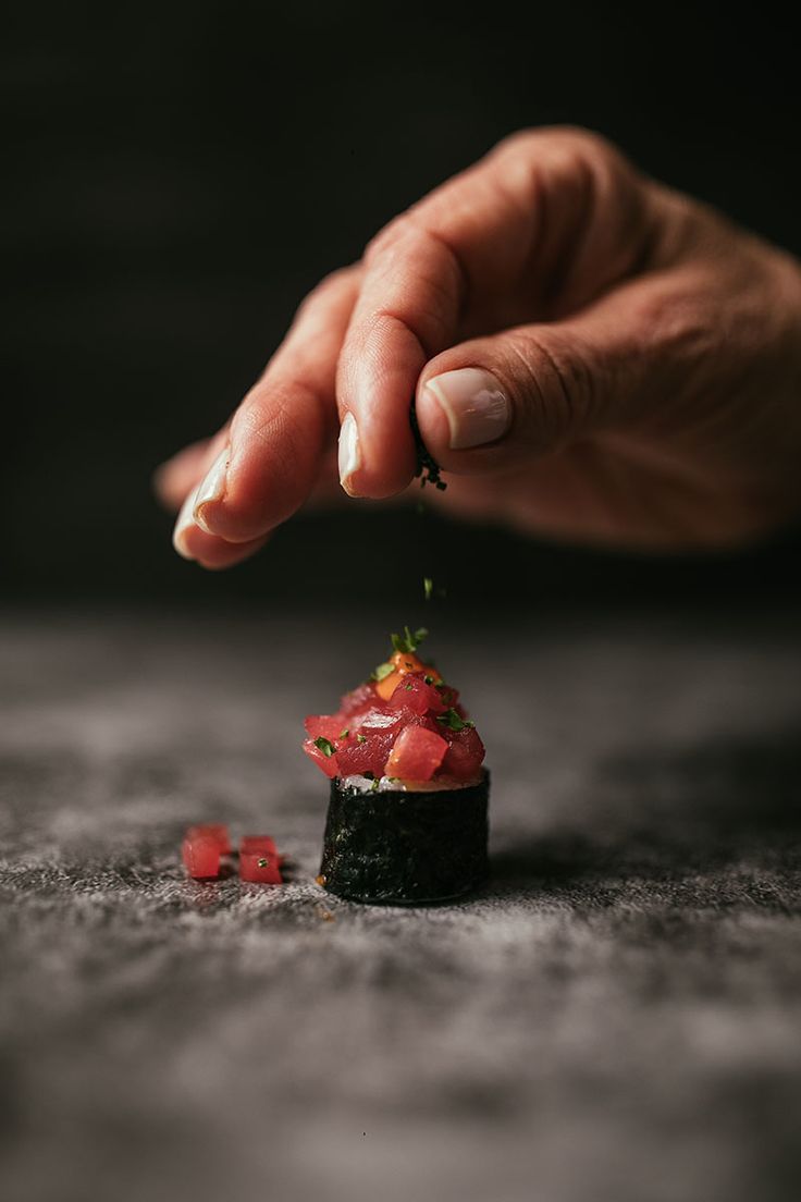 a hand reaching for some food on top of a piece of sushi with strawberries