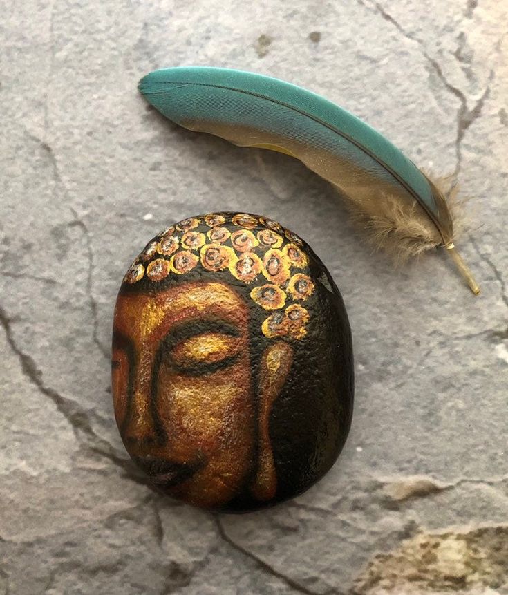 a rock with a painted buddha face next to a feather