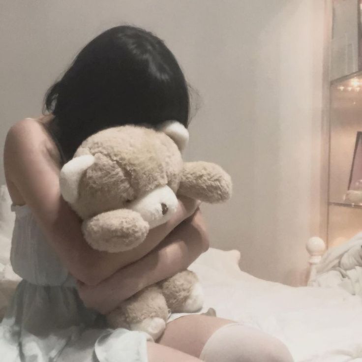 a woman sitting on a bed holding a teddy bear in her arms and looking at the camera