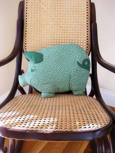 a green pig pillow sitting on top of a wooden chair with wicker backrest