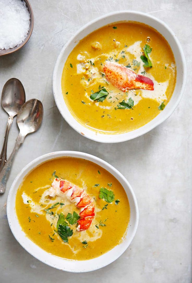 two bowls of soup with lobster and parsley on top, one bowl is yellow