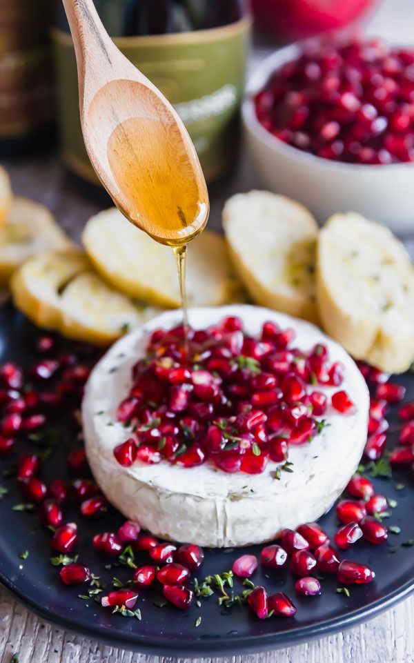 a wooden spoon drizzling pomegranate onto a piece of cheese