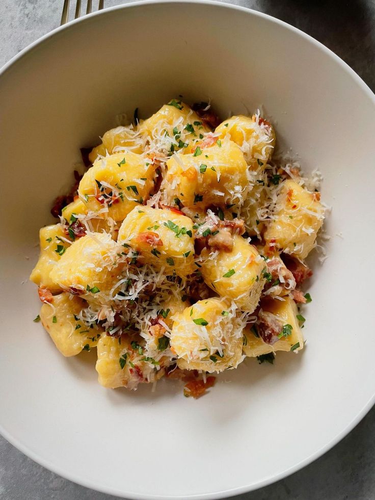 a white bowl filled with pasta covered in parmesan cheese and garnished with herbs