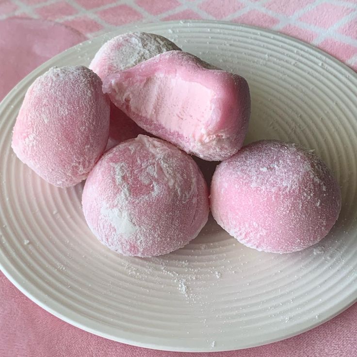 four pink marshmallows on a white plate next to a pink tablecloth