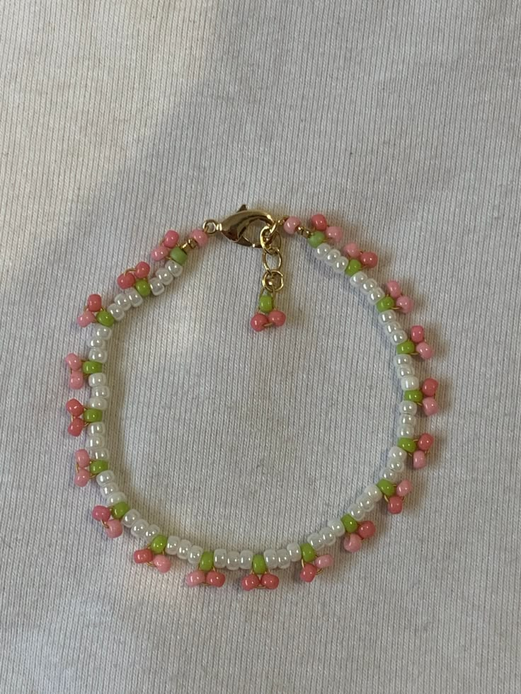 a pink and green beaded bracelet on a white surface with a gold charm hanging from the clasp