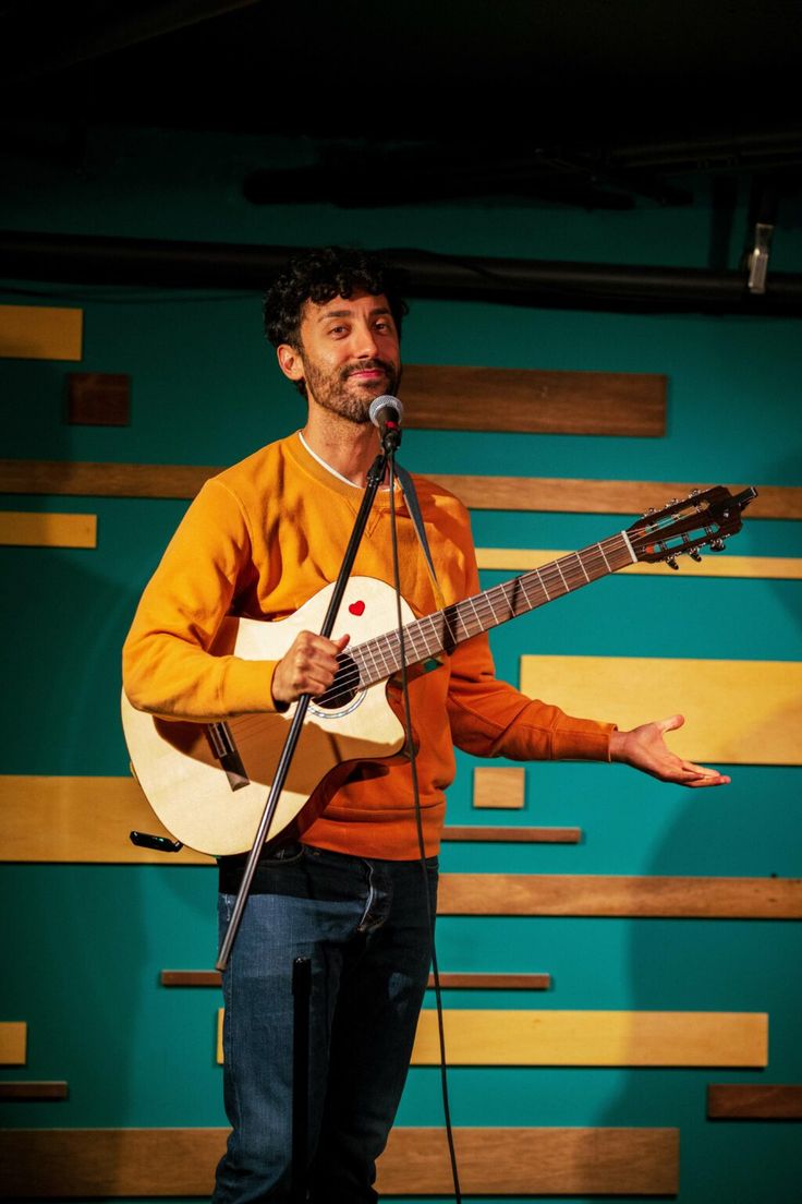 a man standing in front of a microphone while holding a guitar