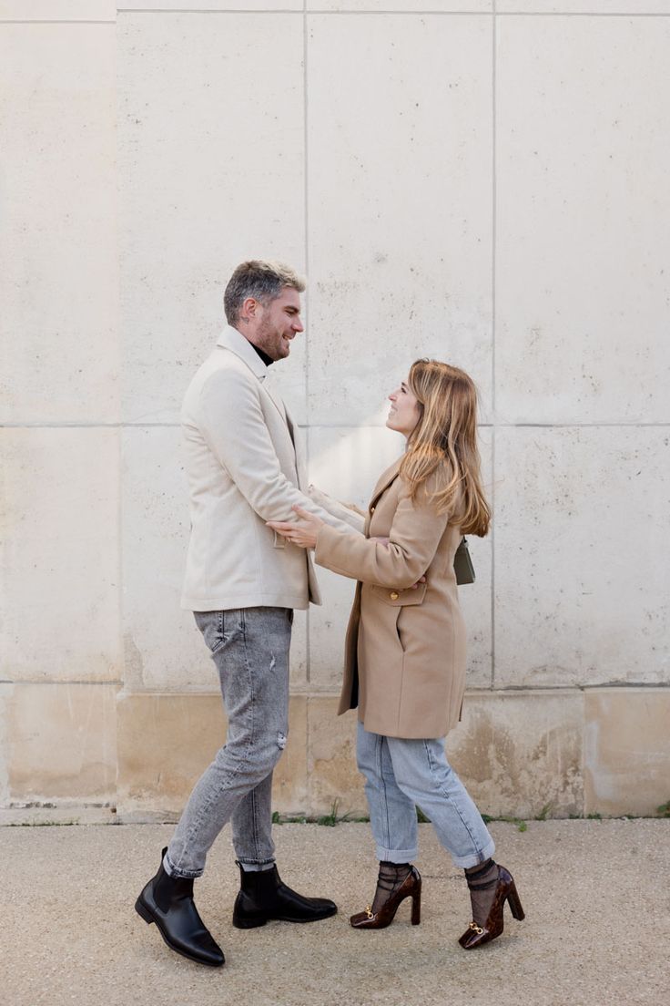 a man and woman holding hands while standing next to each other in front of a wall