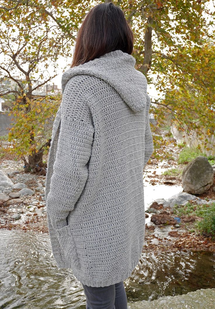 a woman standing in front of a river wearing a gray sweater and grey leggings