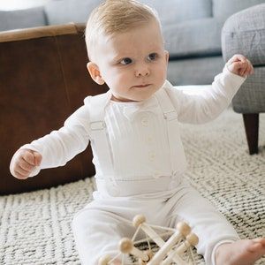 a baby is sitting on the floor playing with a wooden structure and looking at the camera