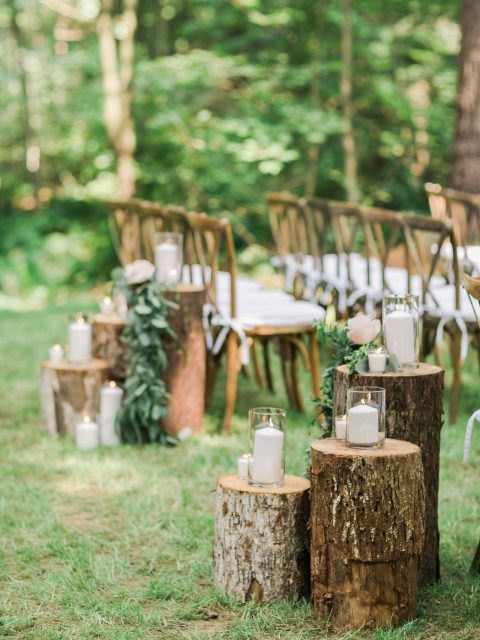 an outdoor wedding setup with candles, flowers and greenery on wooden stumps in the grass