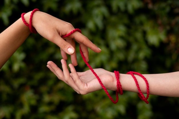 two hands are tied together with red string and another hand is reaching out to the other