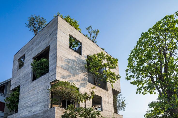 the building has many windows and plants growing on it's sides, as well as trees