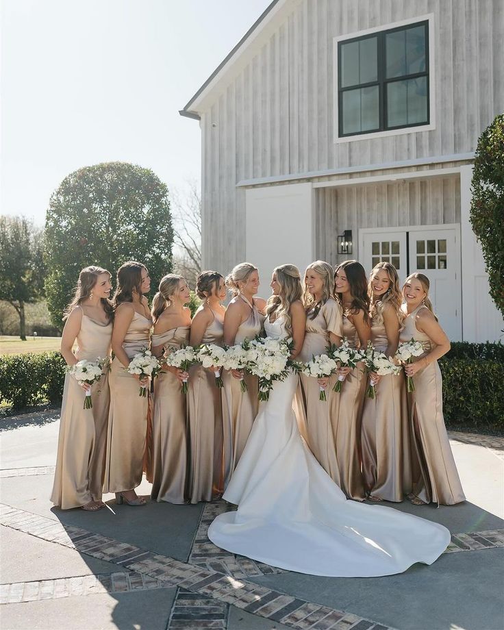 a group of women standing next to each other in front of a white building and holding bouquets