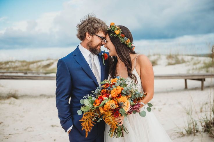 a bride and groom standing together on the beach with their bouquets in front of them