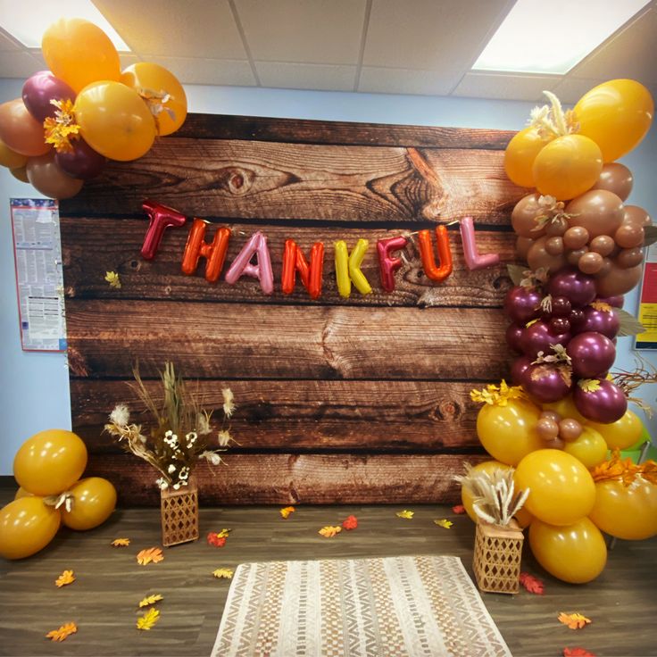 a thank you sign surrounded by balloons and streamers in front of a wooden wall