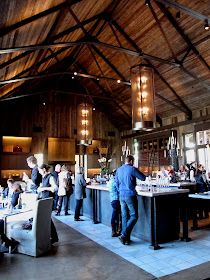 a group of people standing around a bar in a room with wooden walls and ceilings