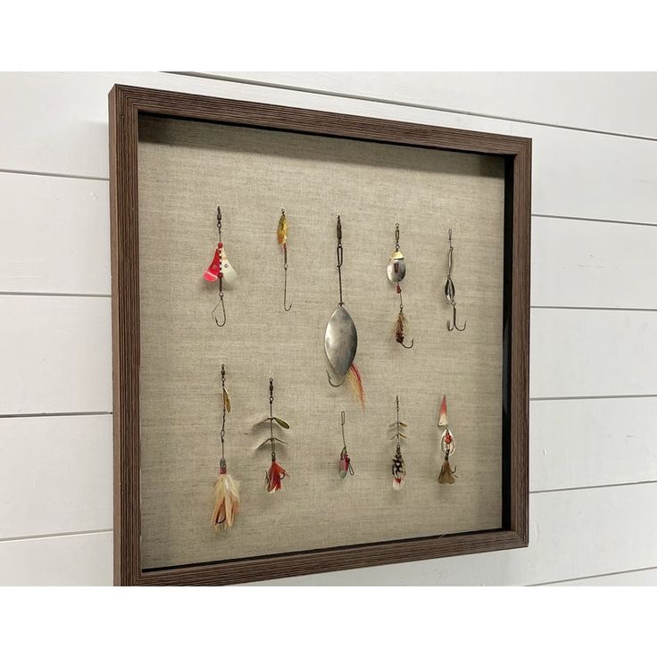 a shadow frame with fishing hooks and spoons hanging from it's sides on the wall