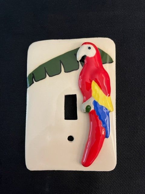 a red and yellow parrot sitting on top of a white light switch cover with palm leaves