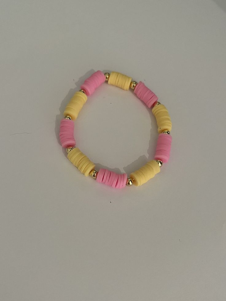 a pink and yellow beaded bracelet on a white surface with gold beads in the middle