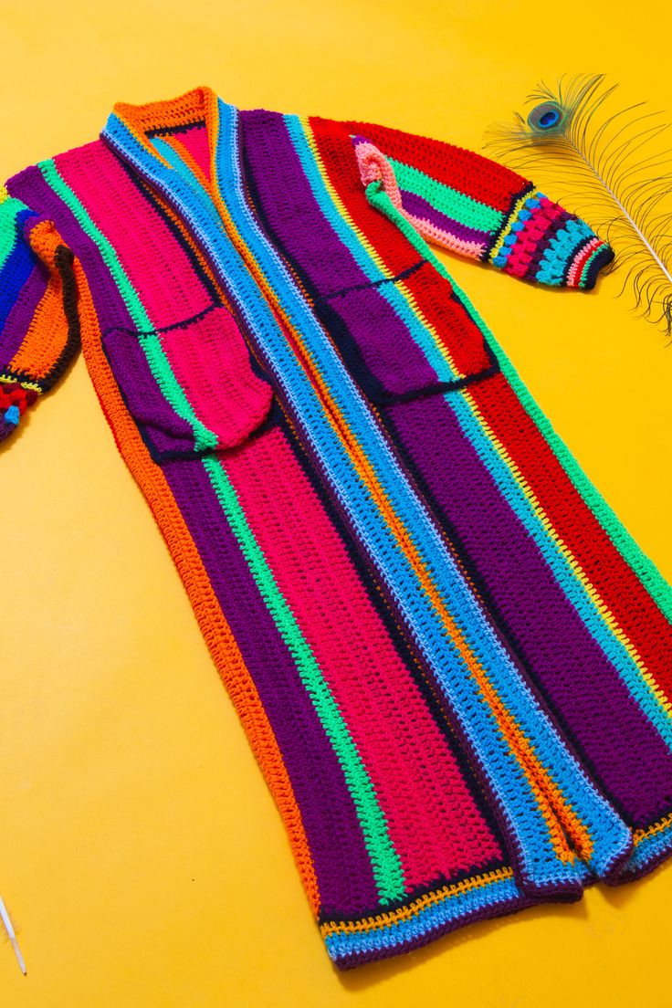 a multicolored sweater laying on top of a yellow table next to a feather