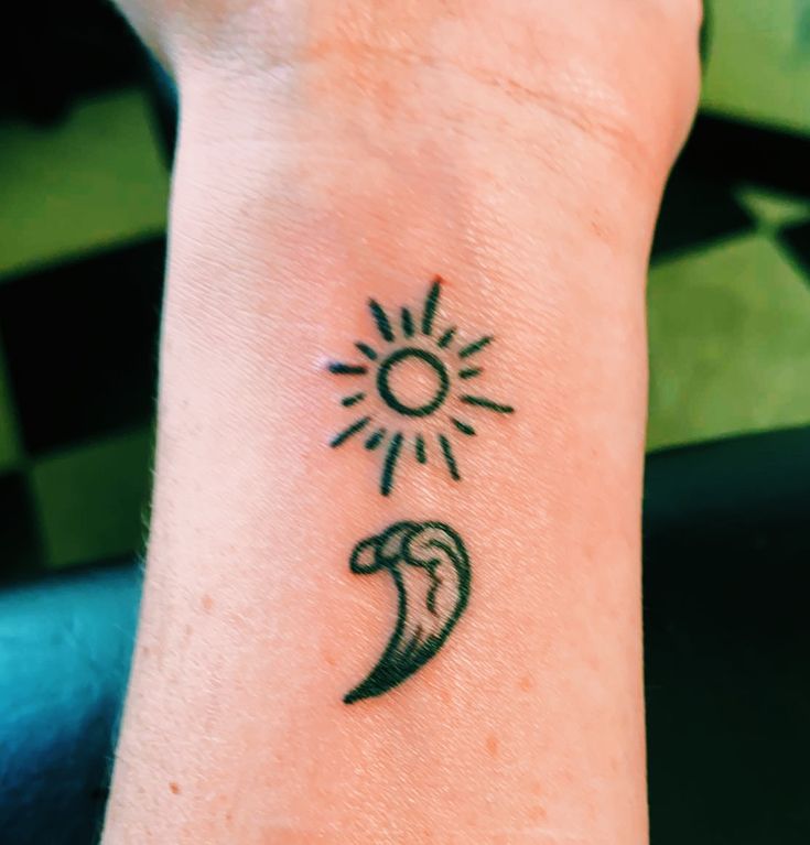 a person's wrist with a tattoo on it that has an image of a sun and a wave