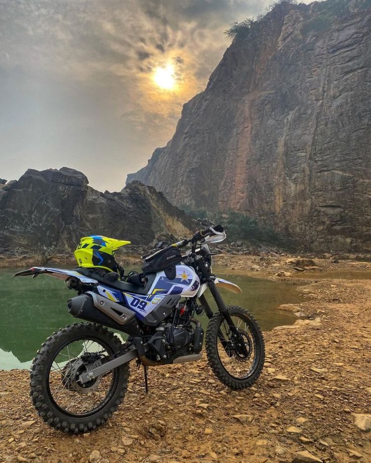 a motorcycle parked on the side of a dirt road next to a body of water