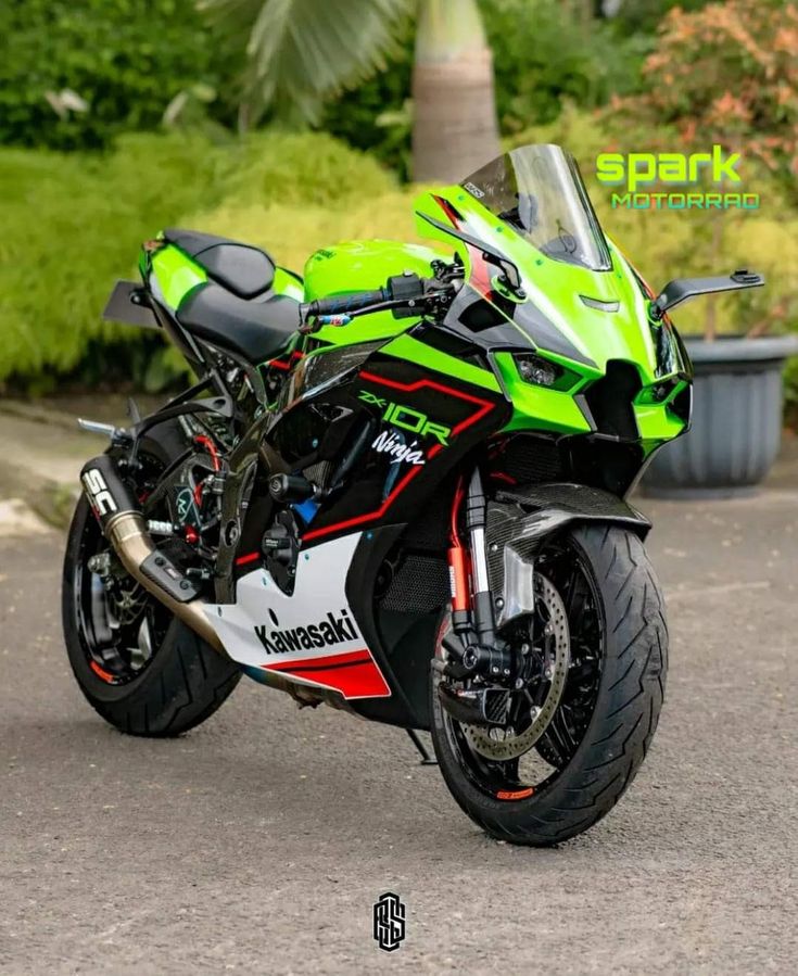 a green and black motorcycle parked on the side of the road in front of some bushes