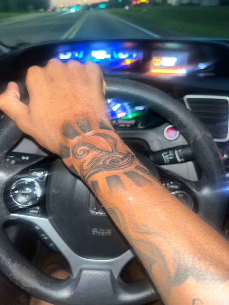 a man driving a car with a tattoo on his arm and hand behind the steering wheel