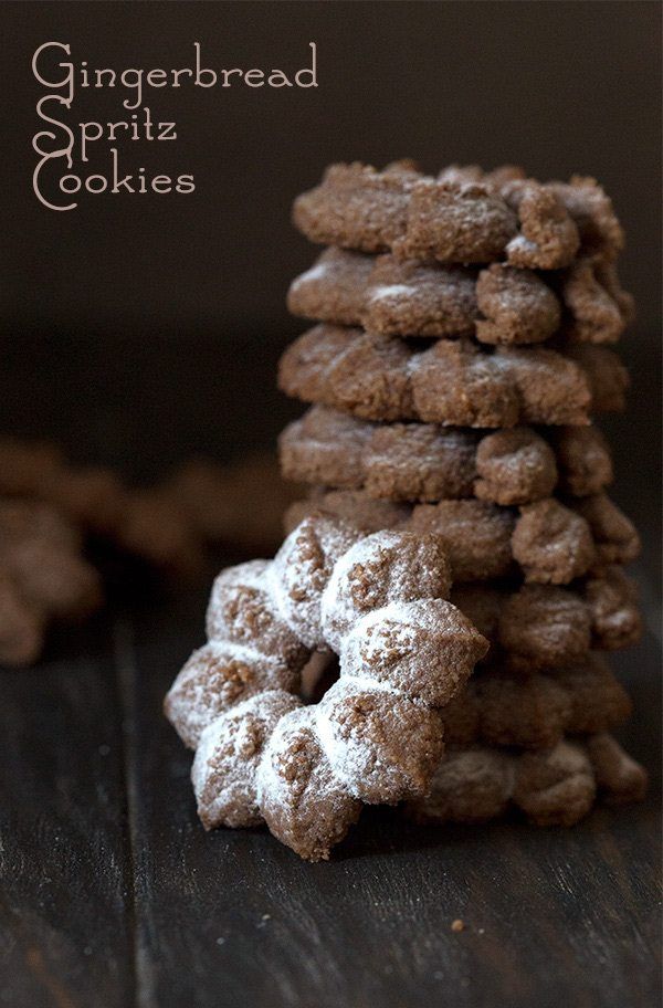 a stack of gingerbread spritz cookies on top of a wooden table with powdered sugar